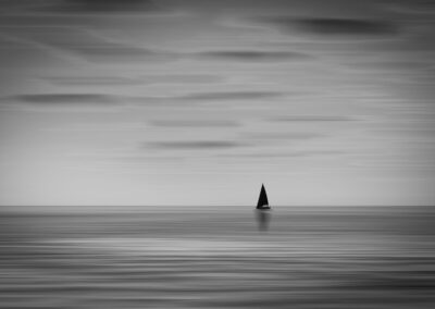 A solitary sailboat crossing calm waters at dusk, the sky streaked with the last warm light of the day.