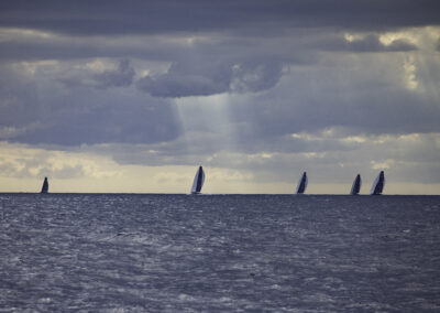 Five racing yachts caught in a single frame, their sails aligned like a fleet in formation.