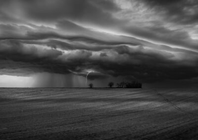 Storm cells like this one can produce sudden lightning strikes and heavy rainfall over open countryside, visible from miles away across flat terrain.